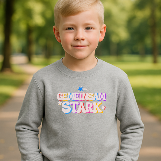 Junge trägt graues Kinder Sweatshirt ‚Gemeinsam stark‘. Buntes Design mit Sternchen – Statement für Zusammenhalt, Vielfalt & Inklusion.“