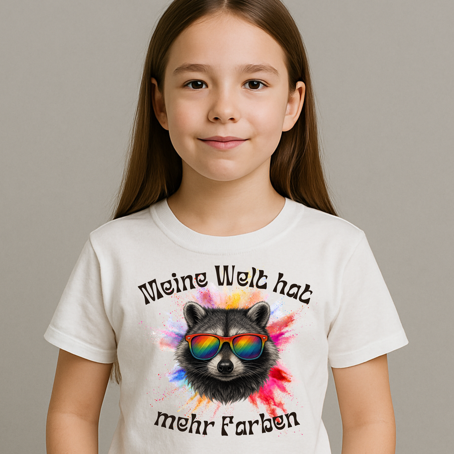 Mädchen trägt weißes Kinder T-Shirt ‚Meine Welt hat mehr Farben‘ mit buntem Waschbär. Fröhliches Statement für Vielfalt & Anderssein.